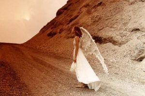 Anielica, w białej suknii, idzie kamienistą drogą.